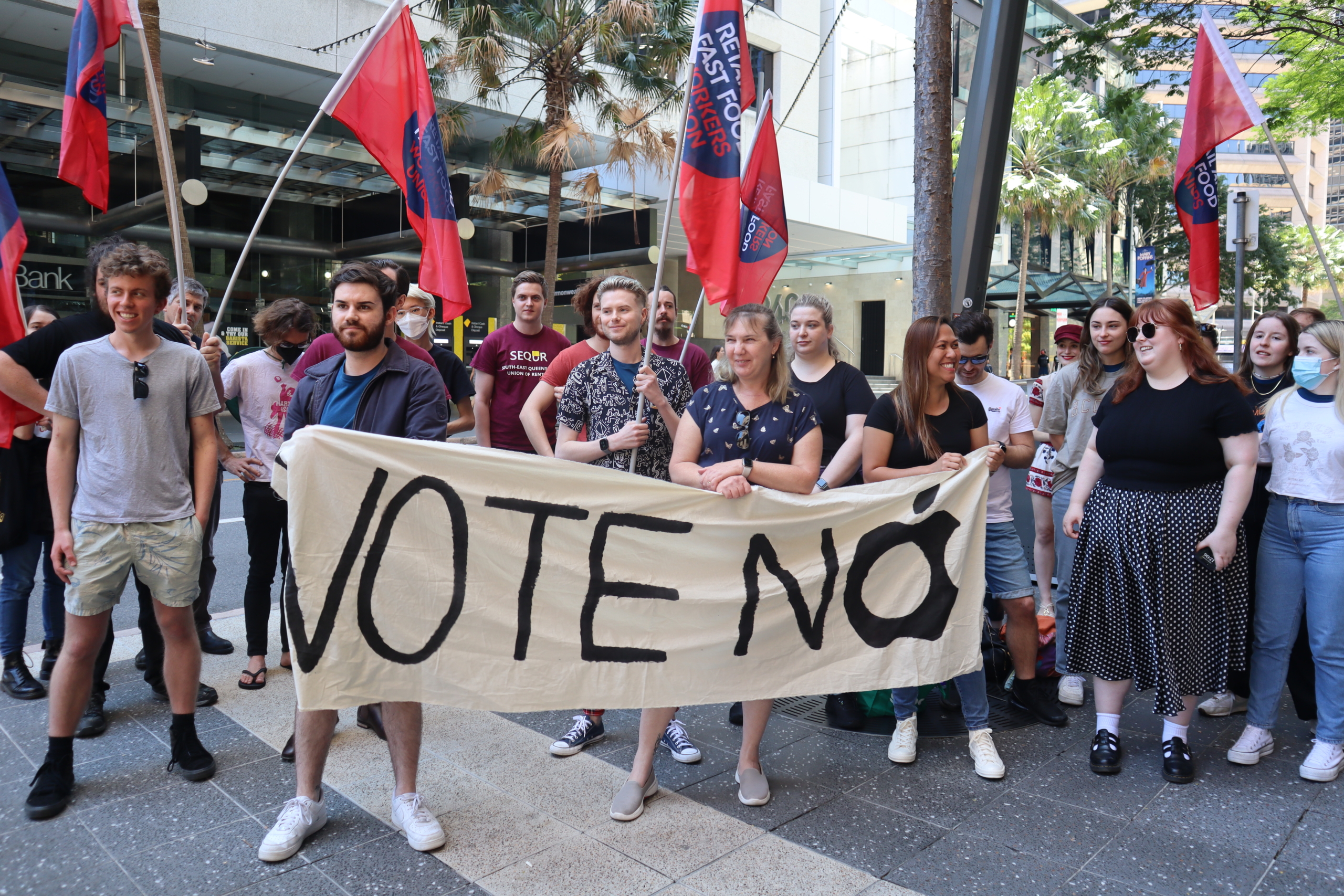A photograph of striking Apple workers with union flags and a banner that says "Vote No".